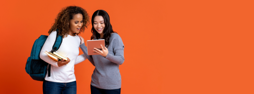 A young Black woman and a young Asian woman looking at a tablet smiling.