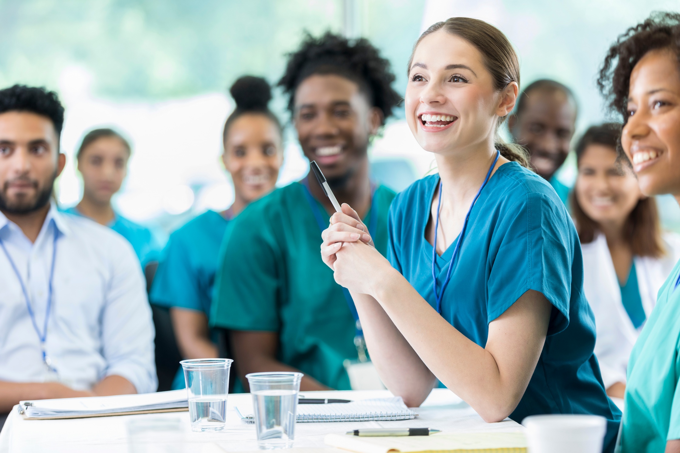 health residents listening to an instructor or speaker with pens and paper for note-taking nearby